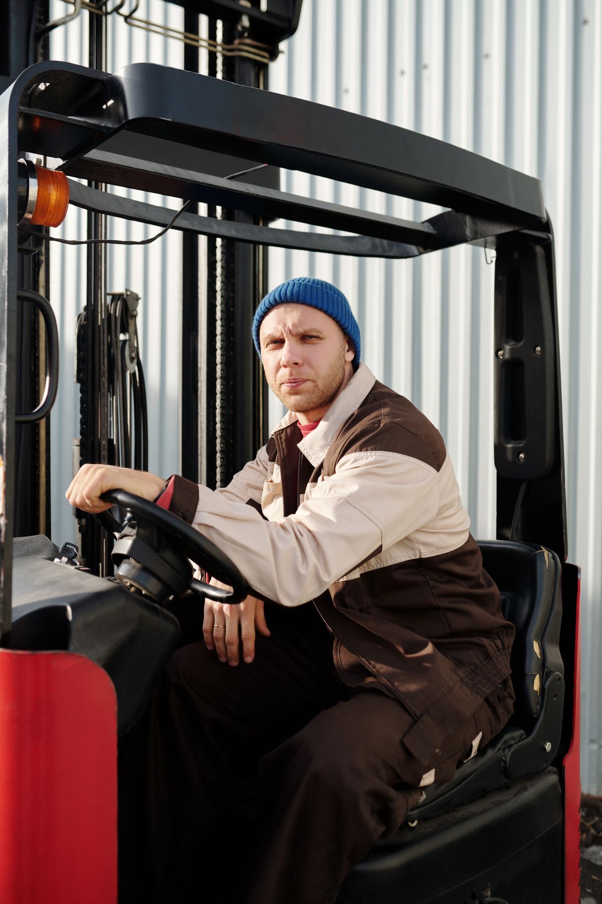 Forklift operator in a beanie working near an industrial building